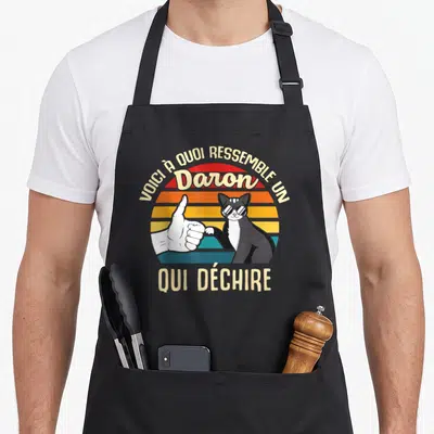 Tablier de cuisine noir avec illustration vintage d'un chat aux lunettes et une main faisant un pouce levé sur fond de soleil rayé.