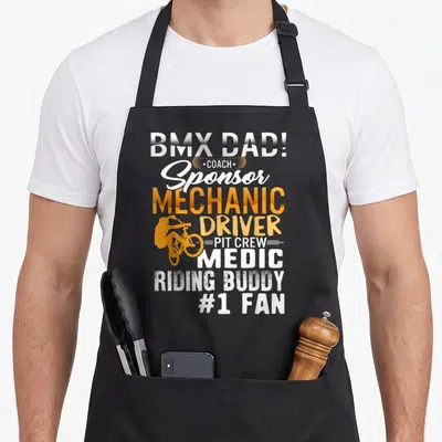 Tablier de cuisine noir avec typographie orange et blanche listant les rôles d'un papa cycliste BMX.