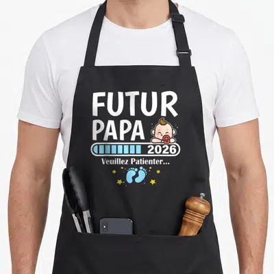 Tablier de cuisine noir avec inscription Futur Papa 2026 et illustration de bébé tenant un doudou rouge.
