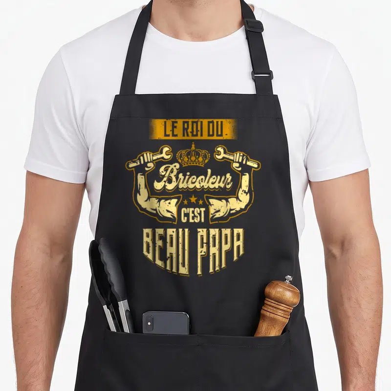 Tablier de cuisine noir avec illustration jaune et orange représentant un roi bricoleur et la mention beau papa.