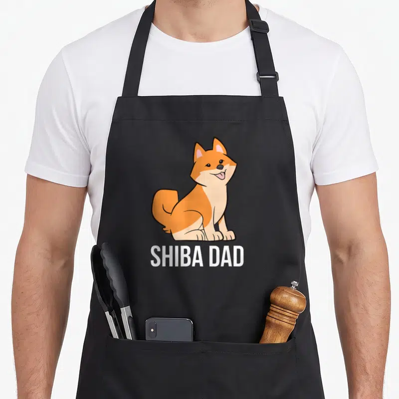 Tablier de cuisine noir avec un Shiba Inu assis souriant et le texte Shiba Dad en blanc.