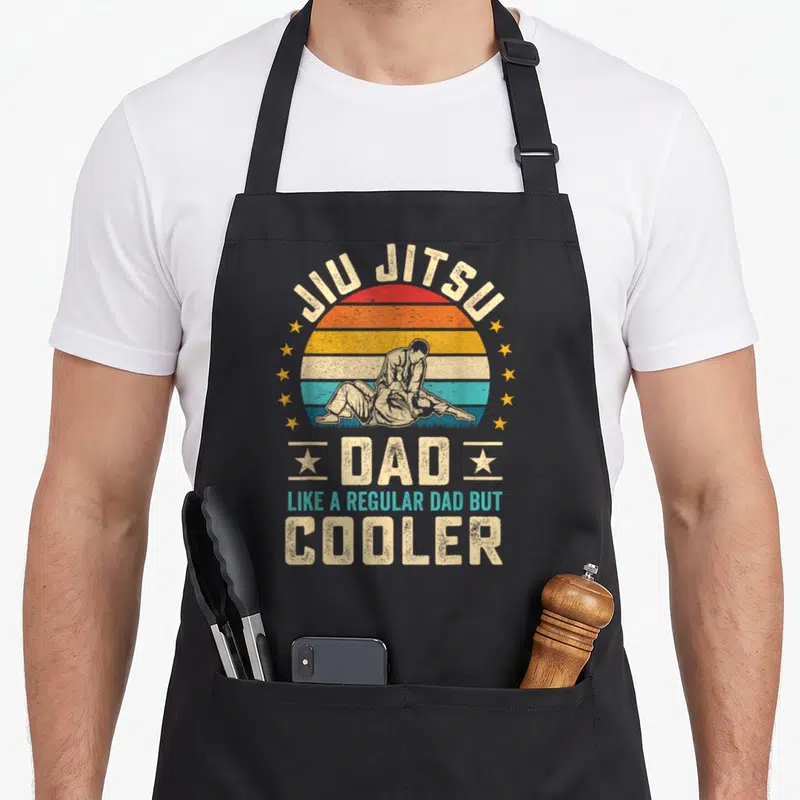 Tablier de cuisine noir avec illustration vintage Jiu Jitsu Dad et texte like a regular dad but cooler entouré d'étoiles jaunes.