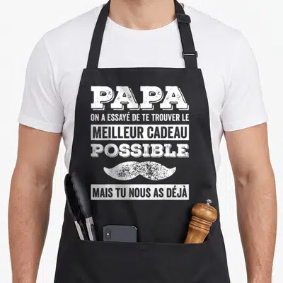 Tablier de cuisine noir avec texte blanc Papa et moustache stylisée sur fond uni.