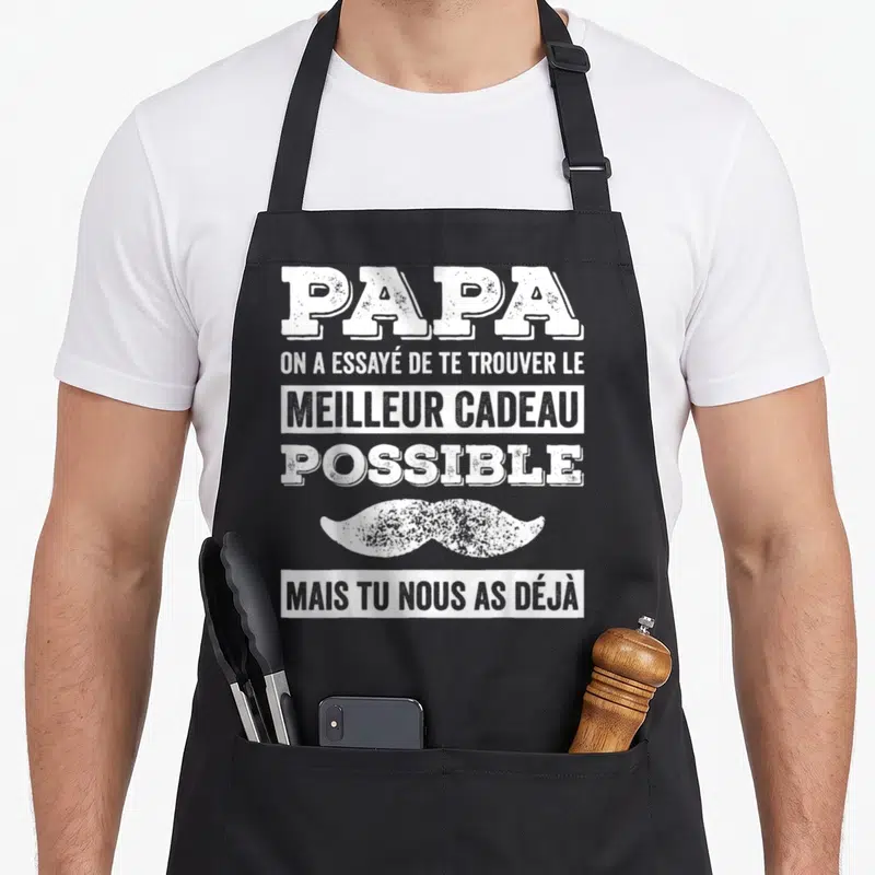 Tablier de cuisine noir avec texte blanc Papa et moustache stylisée sur fond uni.