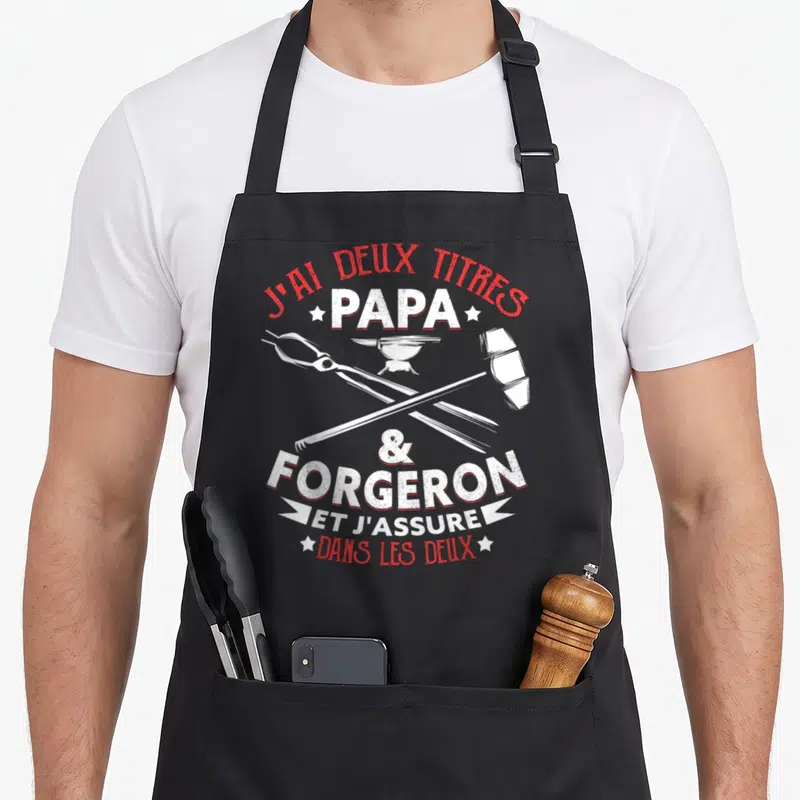 Tablier de cuisine noir avec inscription Papa Forgeron, enclume, marteau et pince croisés en blanc et rouge.