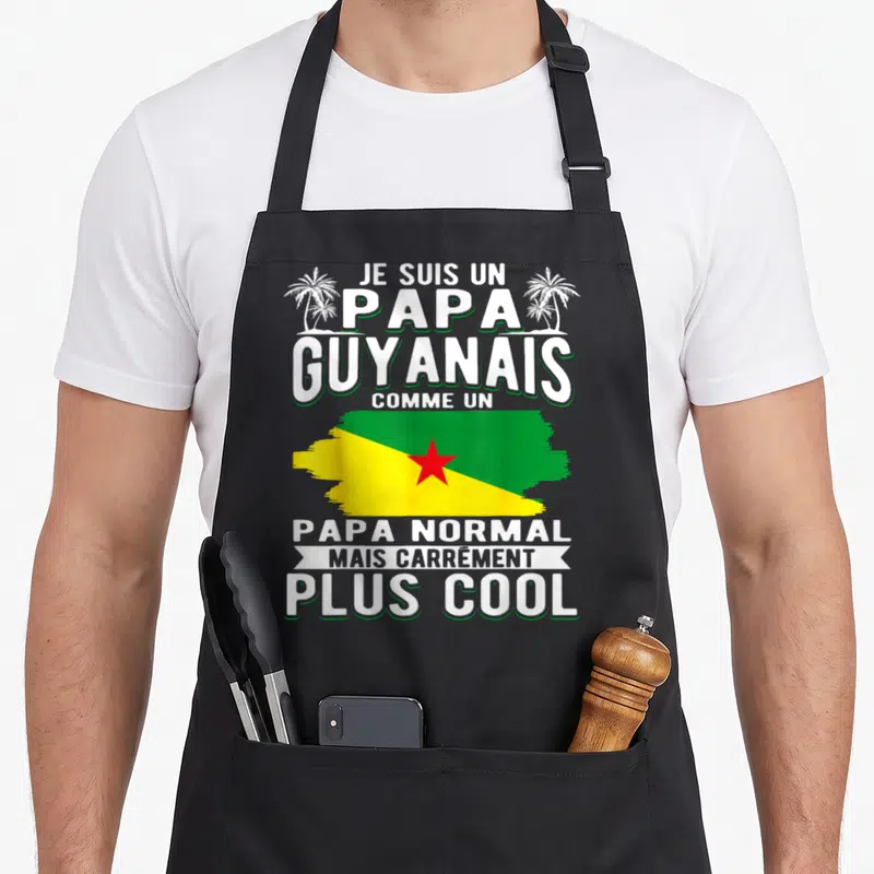 Tablier de cuisine noir avec l'inscription Je Suis Un Papa Guyanais et le drapeau du Guyana sur fond blanc et vert.