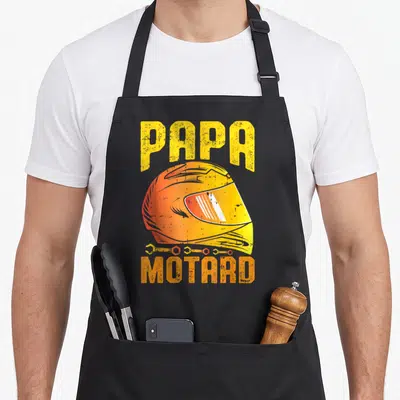 Tablier de cuisine noir avec illustration de casque de moto et texte Papa Motard en lettres jaunes et oranges.