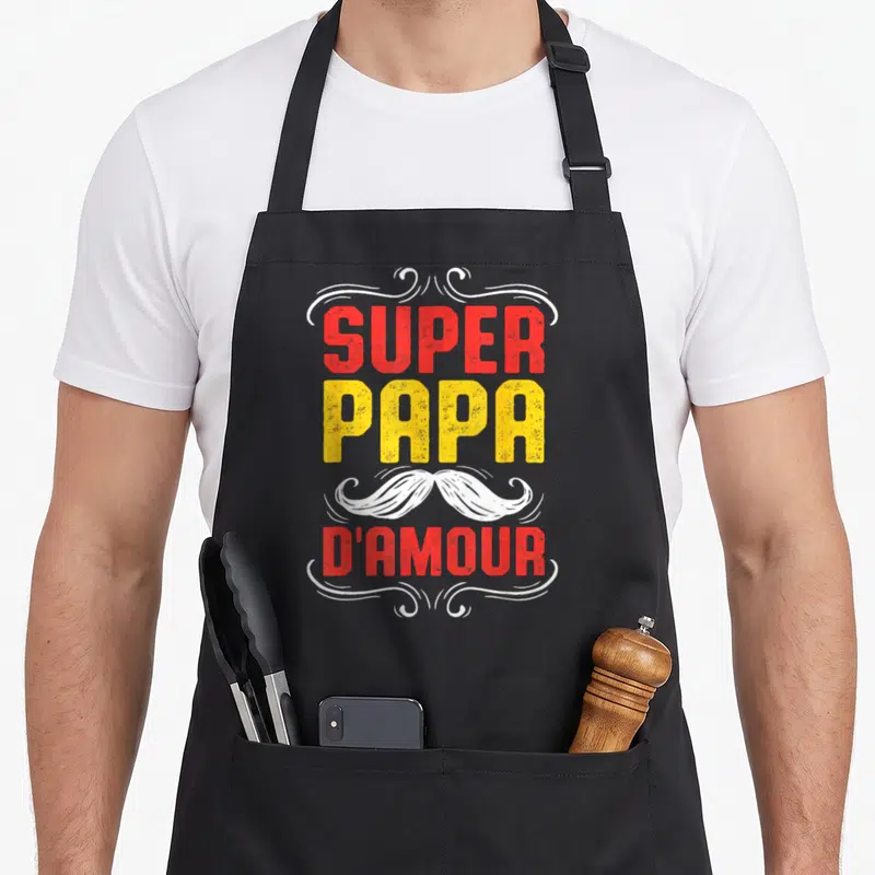 Tablier de cuisine noir avec texte super papa d'amour et moustache blanche stylisée au centre.
