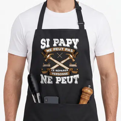 Tablier de cuisine noir avec deux marteaux croisés et l'inscription Si papy ne peut pas le réparer personne ne peut en blanc et marron.