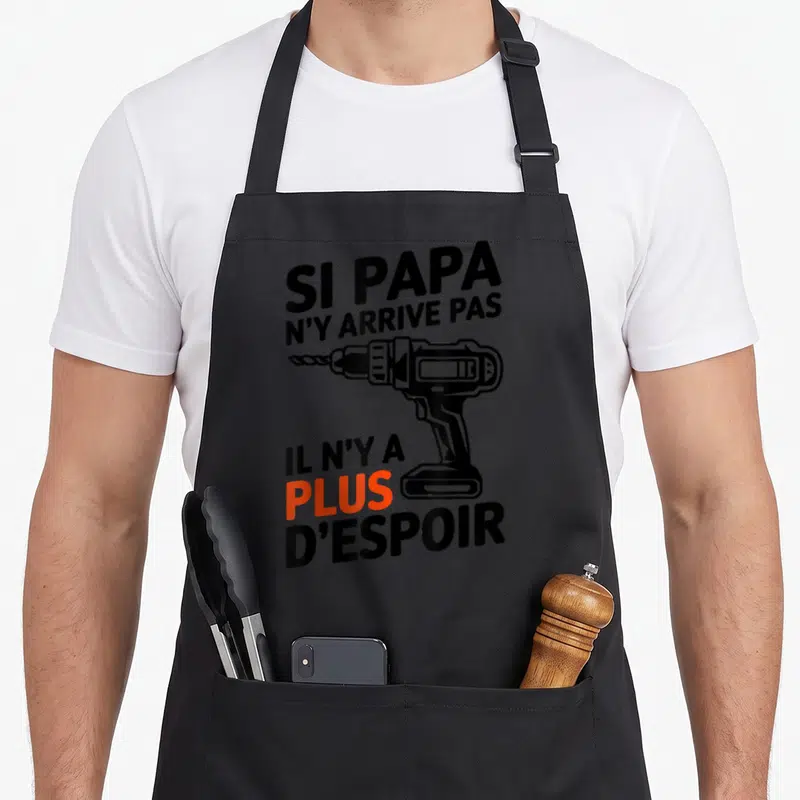 Tablier de cuisine noir avec texte humoristique et illustration de perceuse électrique en noir et orange.