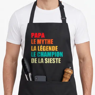 Tablier de cuisine noir avec texte Papa le mythe la légende le champion de la sieste en lettres multicolores stylisées.