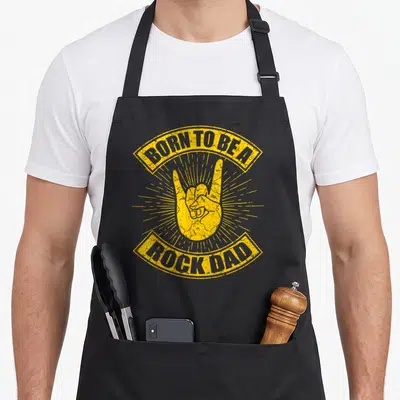 Tablier de cuisine noir avec illustration jaune Born to be a Rock Dad et signe de la main rock.