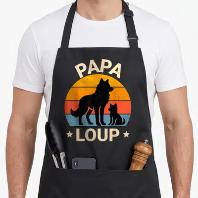Tablier de cuisine noir avec silhouette de loups et texte Papa Loup sur fond de soleil coloré.