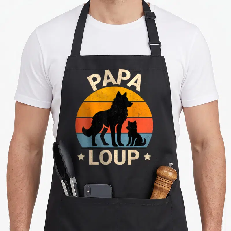 Tablier de cuisine noir avec silhouette de loups et texte Papa Loup sur fond de soleil coloré.