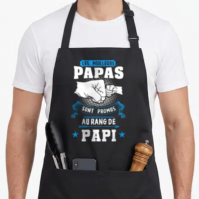 Tablier de cuisine noir avec poings serrés blancs et texte Les meilleurs Papas sont promus au rang de Papi en blanc et bleu.