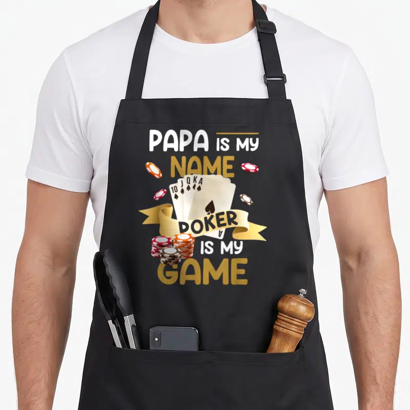 Tablier de cuisine noir avec une illustration de cartes à jouer et des jetons de poker sur fond gris uni.