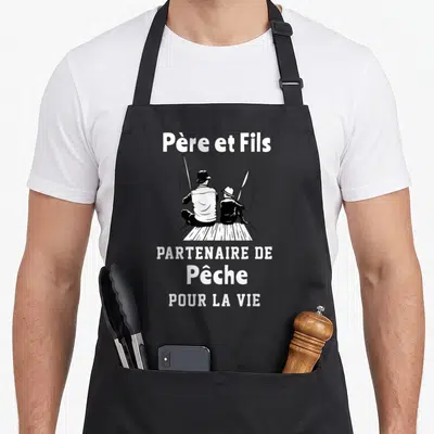 Tablier de cuisine noir avec illustration blanche d'un père et un fils assis en train de pêcher avec des cannes.