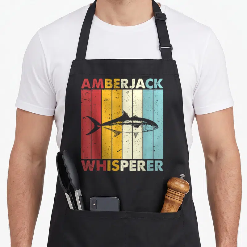 Tablier de cuisine noir avec illustration vintage d'un poisson et texte Amberjack Whisperer sur fond de bandes colorées.