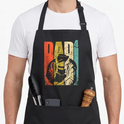 Tablier de cuisine noir avec illustration retro d'un soudeur et le mot DAD 4 en lettres colorées.