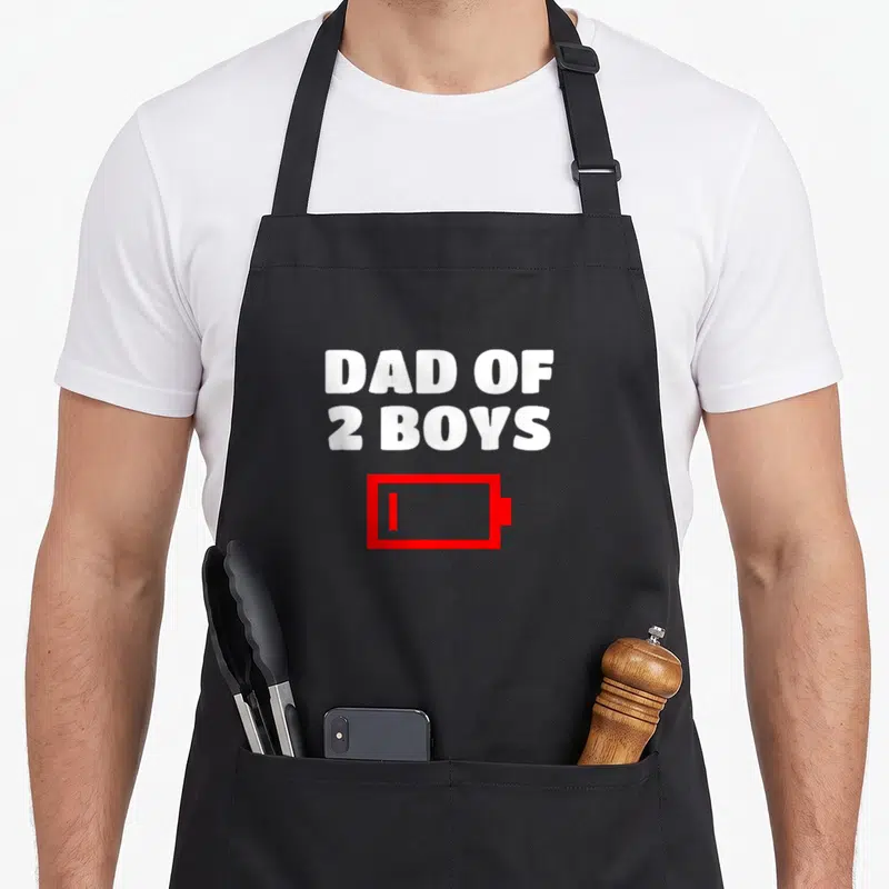 Tablier de cuisine noir avec l'inscription Dad of 2 Boys et une icône de batterie faible rouge en dessous.