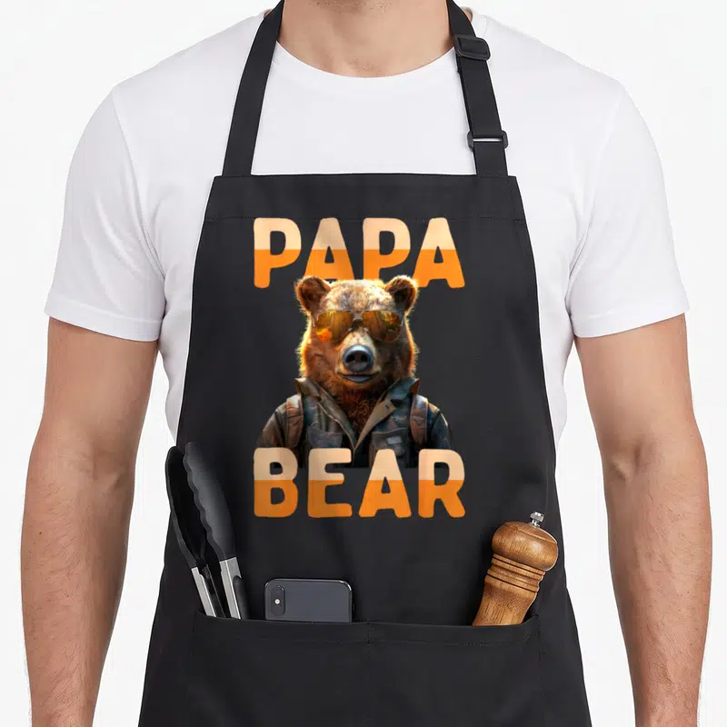 Tablier de cuisine noir avec un ours brun portant des lunettes de soleil et une veste en cuir, encadré par le texte Papa Bear orange.