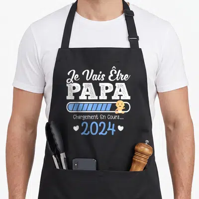 Tablier de cuisine noir avec inscription Je Vais Être PAPA et illustration d'un bébé sur une barre de chargement bleue.