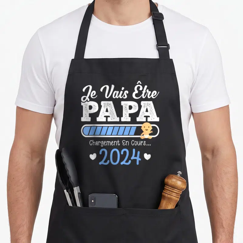 Tablier de cuisine noir avec inscription Je Vais Être PAPA et illustration d'un bébé sur une barre de chargement bleue.