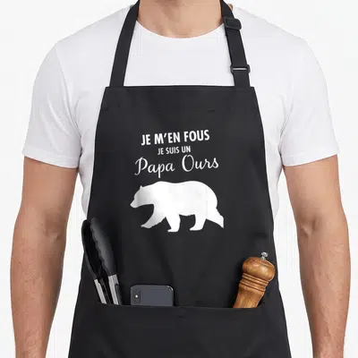 Tablier de cuisine noir avec inscription Je m'en fous je suis un papa ours et silhouette d'ours blanc en bas à droite.