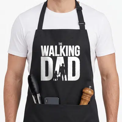Tablier de cuisine noir avec le texte The Walking Dad et une silhouette d'un homme tenant la main d'une petite fille.