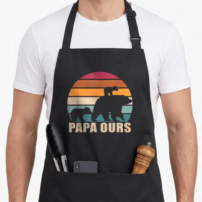 Tablier de cuisine noir avec silhouette d'ours et texte Papa Ours sur fond de soleil rétro.