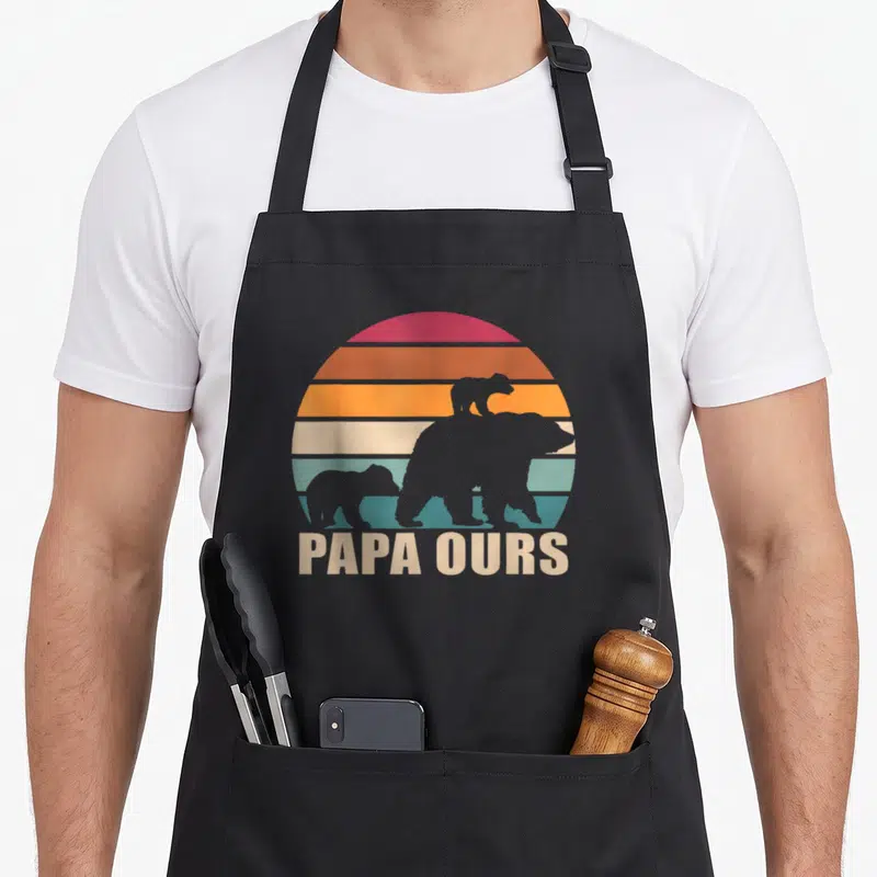 Tablier de cuisine noir avec silhouette d'ours et texte Papa Ours sur fond de soleil rétro.