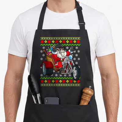 Tablier de cuisine noir avec Père Noël motard sur trike et motifs de tricot festifs.