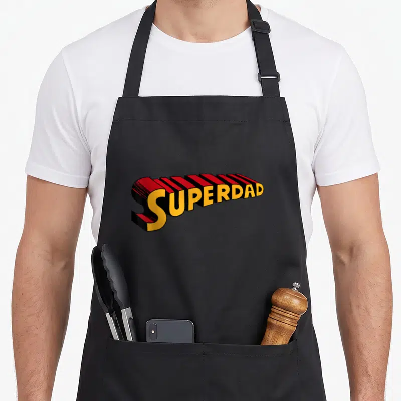 Tablier de cuisine noir avec l'inscription Superdad en typographie 3D rouge et jaune style comics.