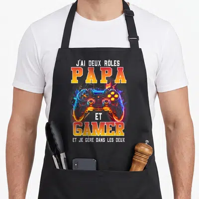 Tablier de cuisine noir avec illustration de manette de jeu colorée et texte Papa et Gamer en lettres orange et jaunes.