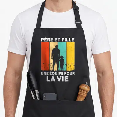 Tablier de cuisine noir avec silhouettes père et fille sur fond de bandes colorées vintage et texte blanc.