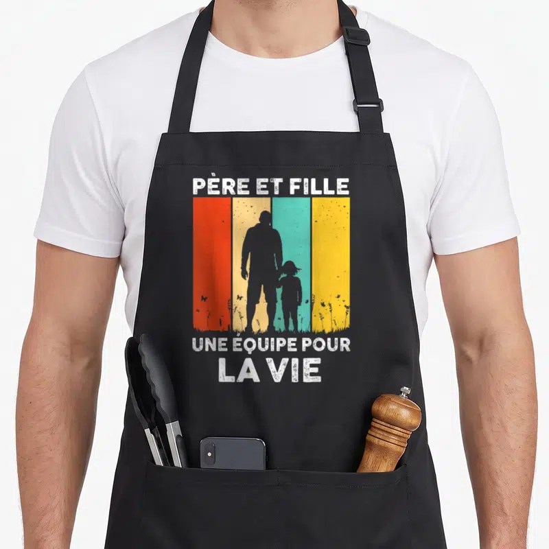 Tablier de cuisine noir avec silhouettes père et fille sur fond de bandes colorées vintage et texte blanc.