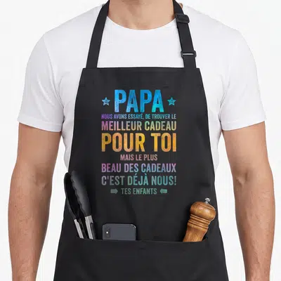 Tablier de cuisine noir avec message coloré sur la paternité et les enfants en typographie dégradée.