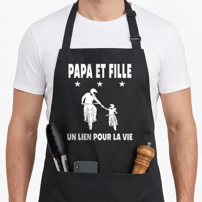 Tablier de cuisine noir avec illustration blanche d'un père et une fille en moto cross sous les mots Papa et fille.