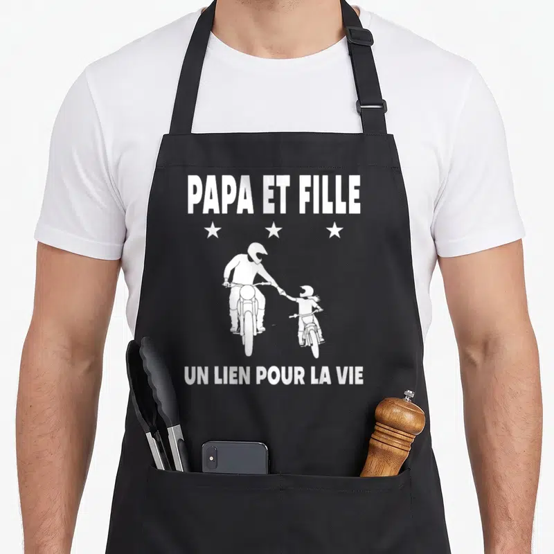 Tablier de cuisine noir avec illustration blanche d'un père et une fille en moto cross sous les mots Papa et fille.