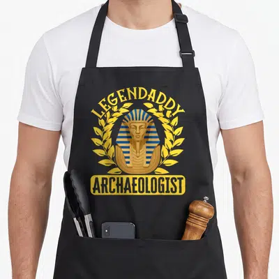 Tablier de cuisine noir avec un pharaon doré et bleu encadré par des feuilles et le texte Legendaddy Archaeologist.