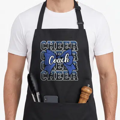 Tablier de cuisine noir avec motif Coach Cheer en nœud bleu pailleté et texte blanc.