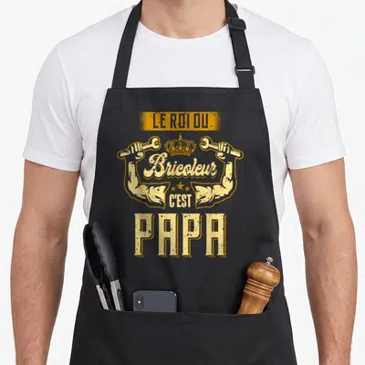 Tablier de cuisine noir avec illustration jaune le roi du bricoleur c'est papa et bras musclés tenant des clés.