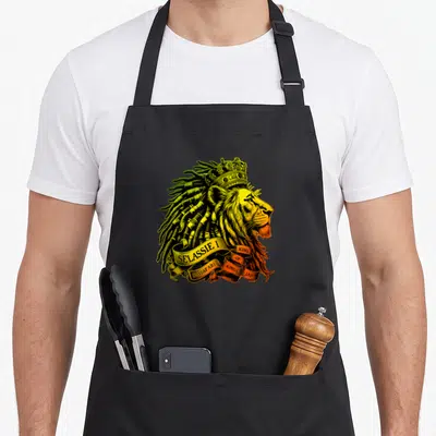 Tablier de cuisine noir avec illustration d'un lion couronné aux cheveux verts et banderoles dorées portant des inscriptions.