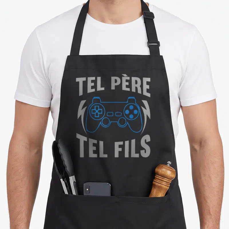 Tablier de cuisine noir avec manette bleue et texte Tel Père Tel Fils en gris clair.