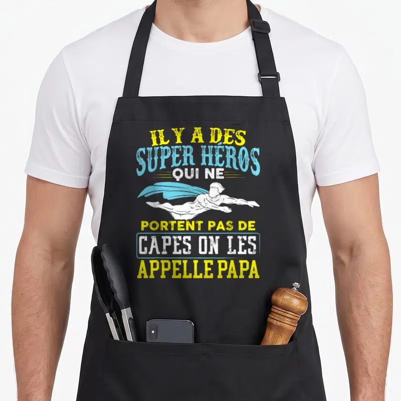Tablier de cuisine noir avec un super héros en vol et le texte Il y a des super héros qui ne portent pas de capes on les appelle papa.