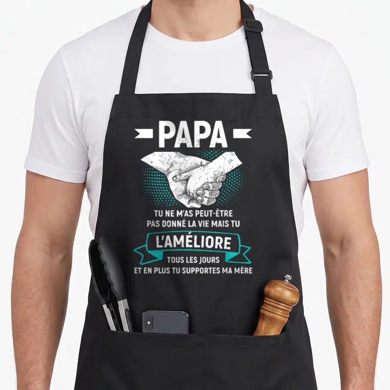 Tablier de cuisine noir avec illustration de mains jointes et texte humoristique sur le rôle de papa dans la famille.