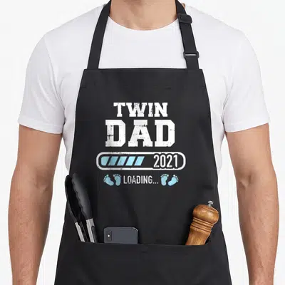 Tablier de cuisine noir avec inscription Twin Dad 2021 Loading et empreintes de pieds bleues.