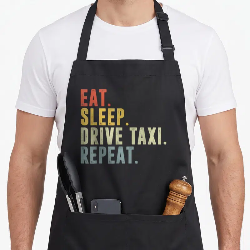Tablier de cuisine noir avec inscription EAT SLEEP DRIVE TAXI REPEAT en lettres orange jaune beige et bleu sur fond uni.