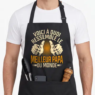 Tablier de cuisine noir avec inscription Voici à quoi ressemble le meilleur papa du monde et deux pouces levés orange et beige.