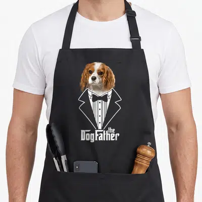 Tablier de cuisine noir avec un Cavalier King Charles Spaniel vêtu d'un costume fumée blanc et le texte The DogFather.